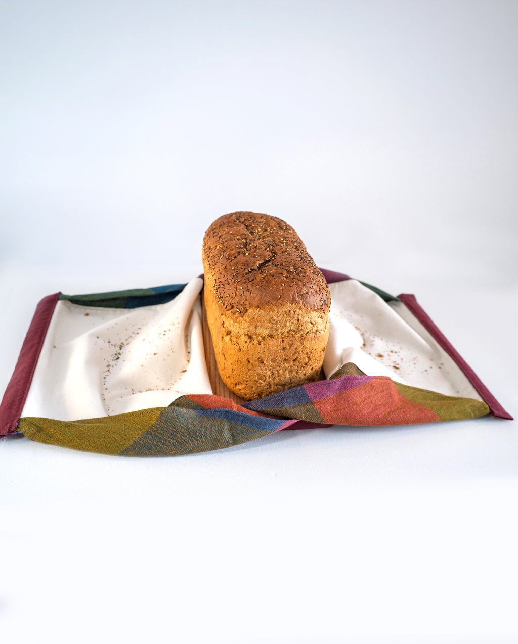Loaf of tin loaf on a wooden slicing board, patterned linen with a white background